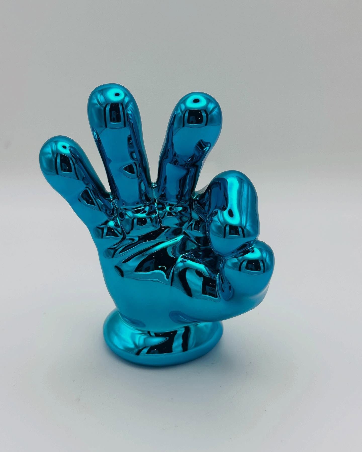 Statua di una mano turchese e lucida, con le dita alzate nel segno