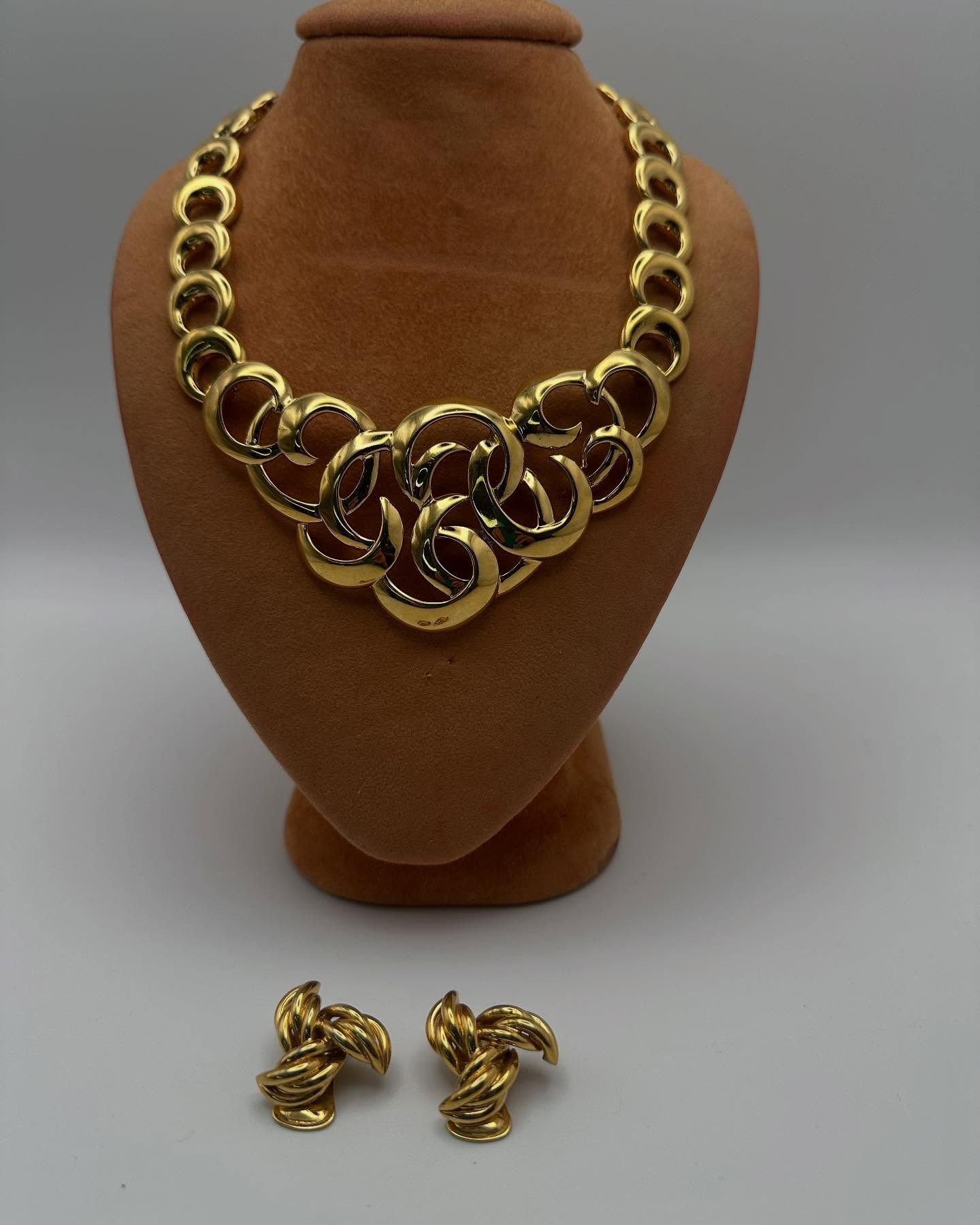 Collana e orecchini color oro su un espositore per gioielli marrone su sfondo bianco.