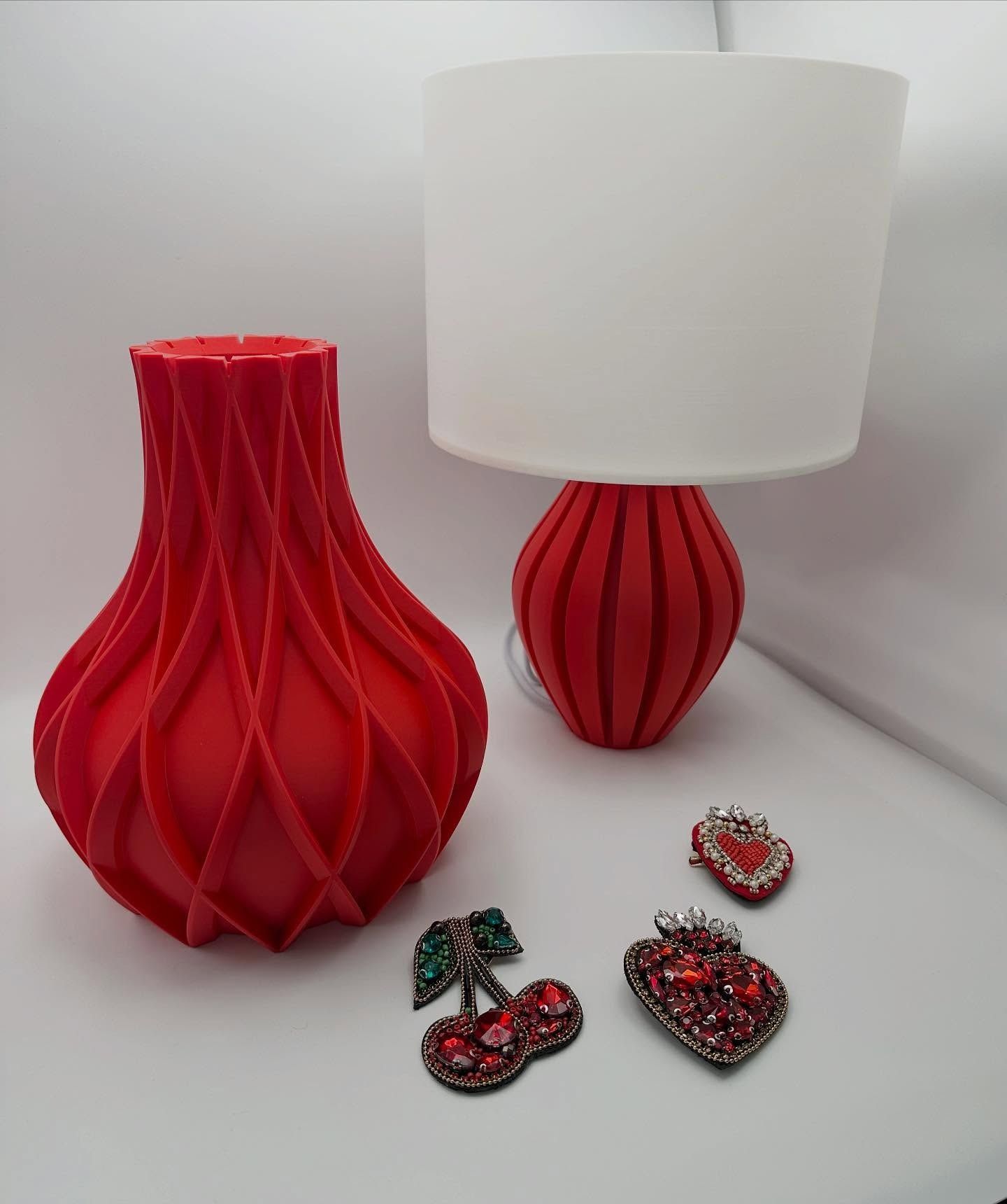 Lampada rossa e vaso accanto a spille scintillanti su una superficie bianca.