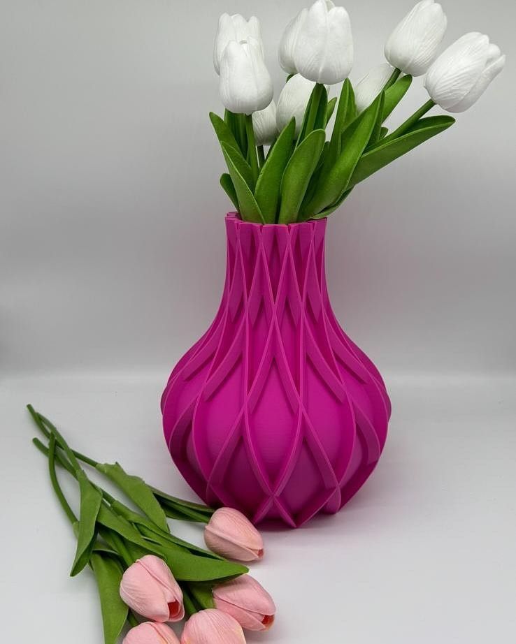 Vaso rosa testurizzato contenente tulipani bianchi, con tulipani rosa adagiati lì vicino su una superficie bianca.