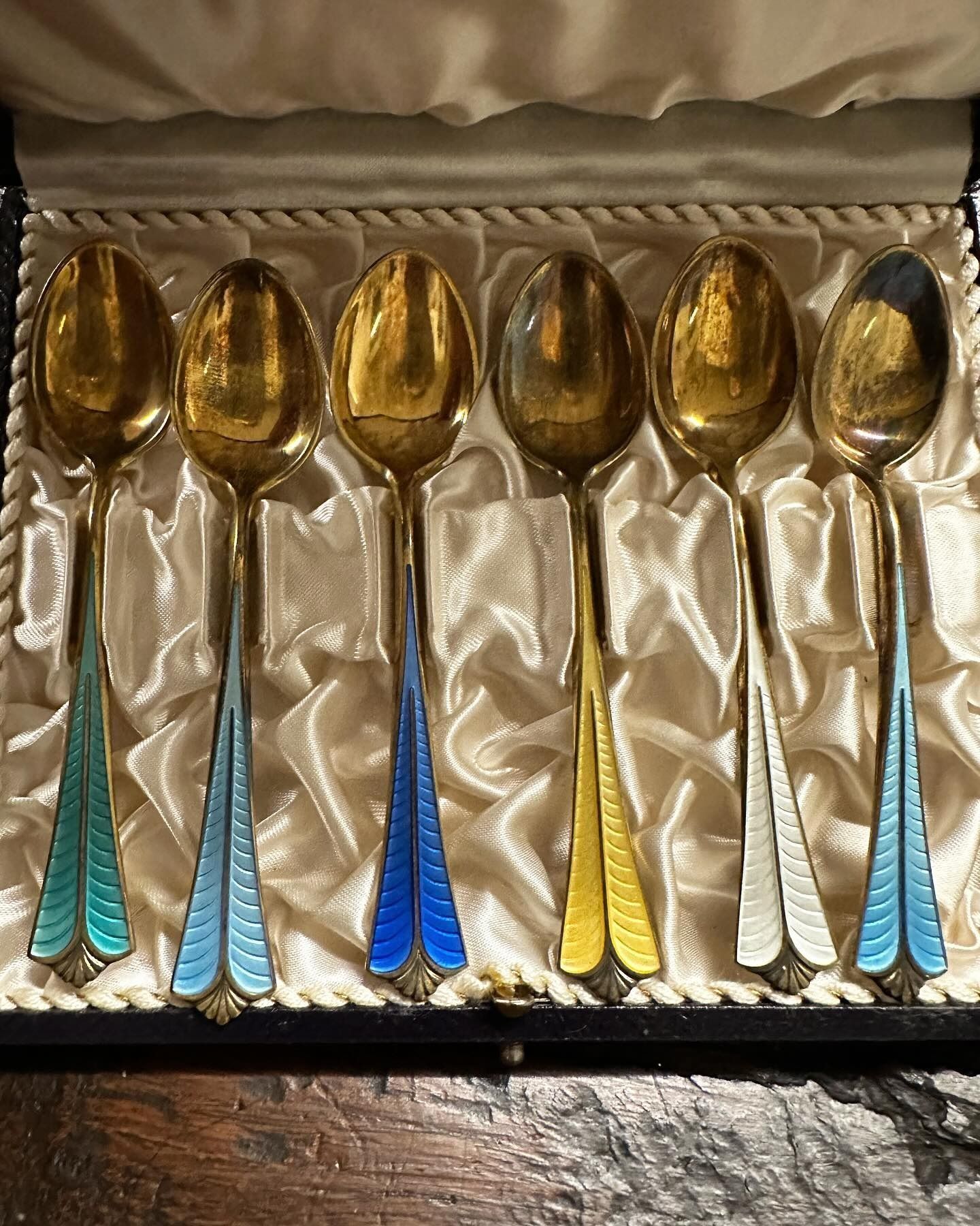 Sei cucchiai d'oro con manici in smalto colorato all'interno di una scatola espositiva.