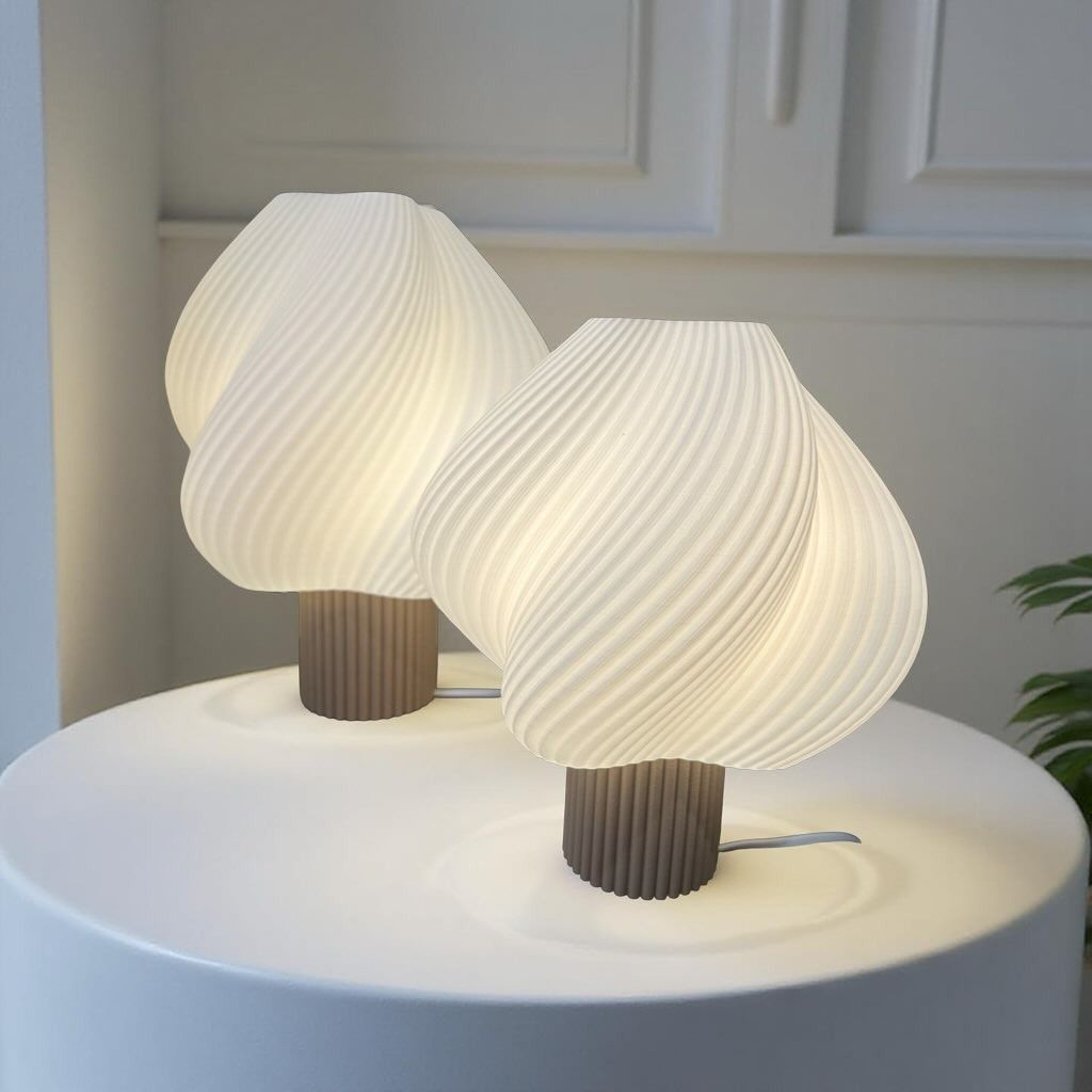 Due lampade da tavolo bianche a forma di spirale su un tavolo bianco con una finestra sullo sfondo.