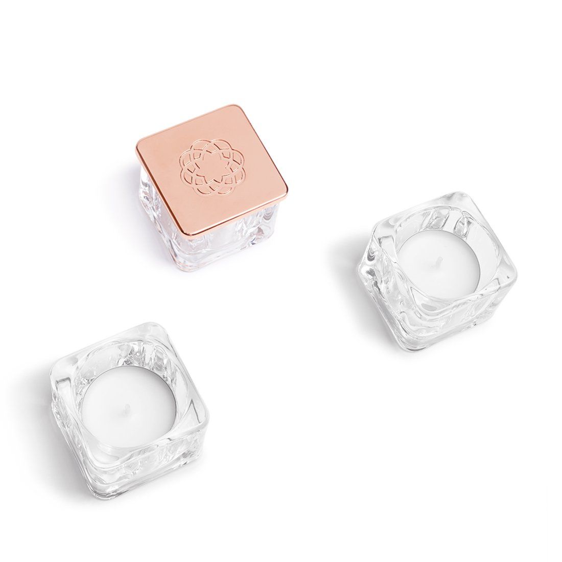 Tre portacandele quadrati con una candela al loro interno su uno sfondo bianco.