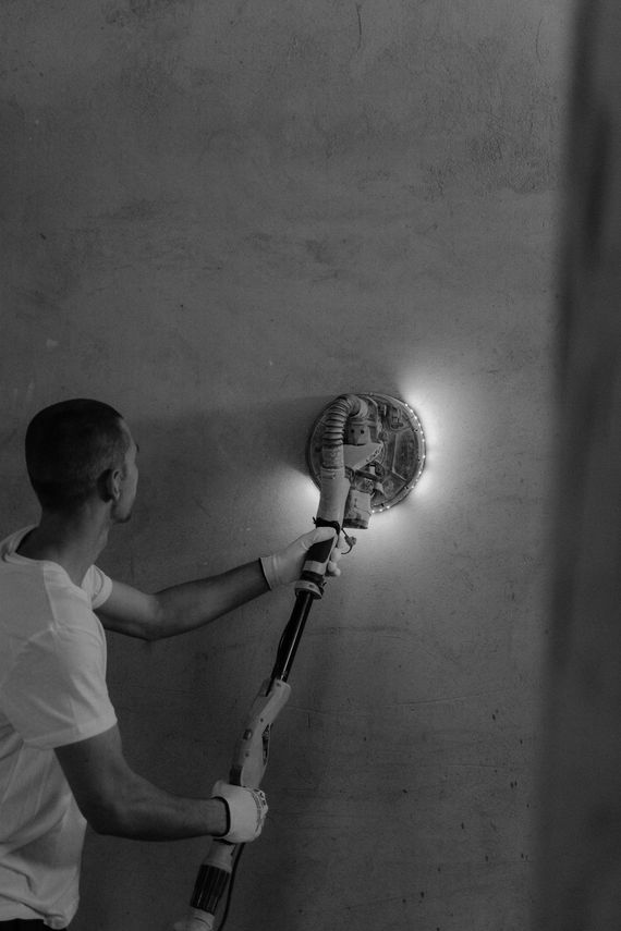 A man is using a sander on a wall in a black and white photo.