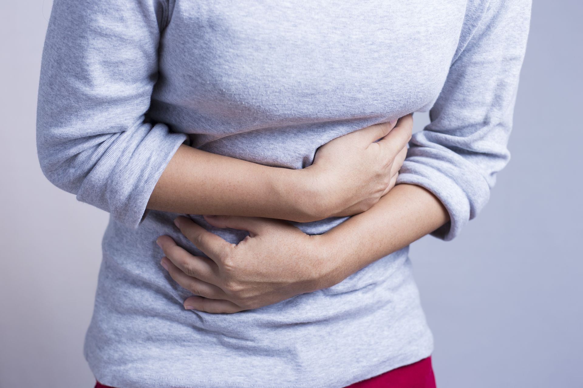 Person holding stomach in pain, wearing a light gray sweater against a plain background