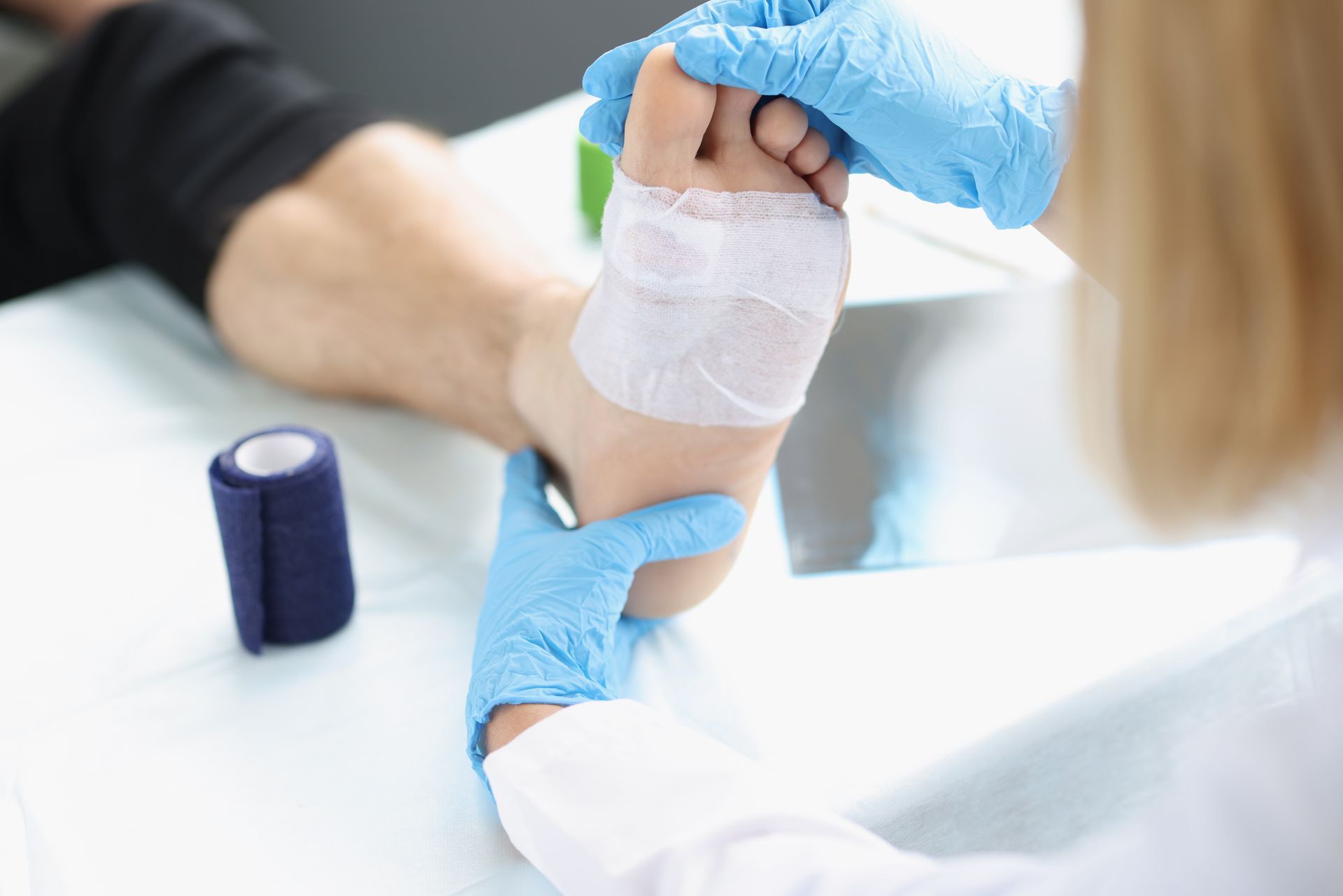 Gloved hands bandaging a patient’s wrist with a white gauze wrap in a clinic setting