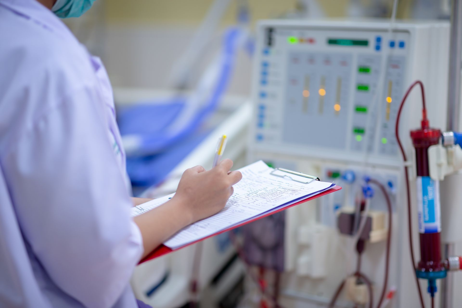 Medical staff writing on a clipboard beside dialysis equipment in a clinic