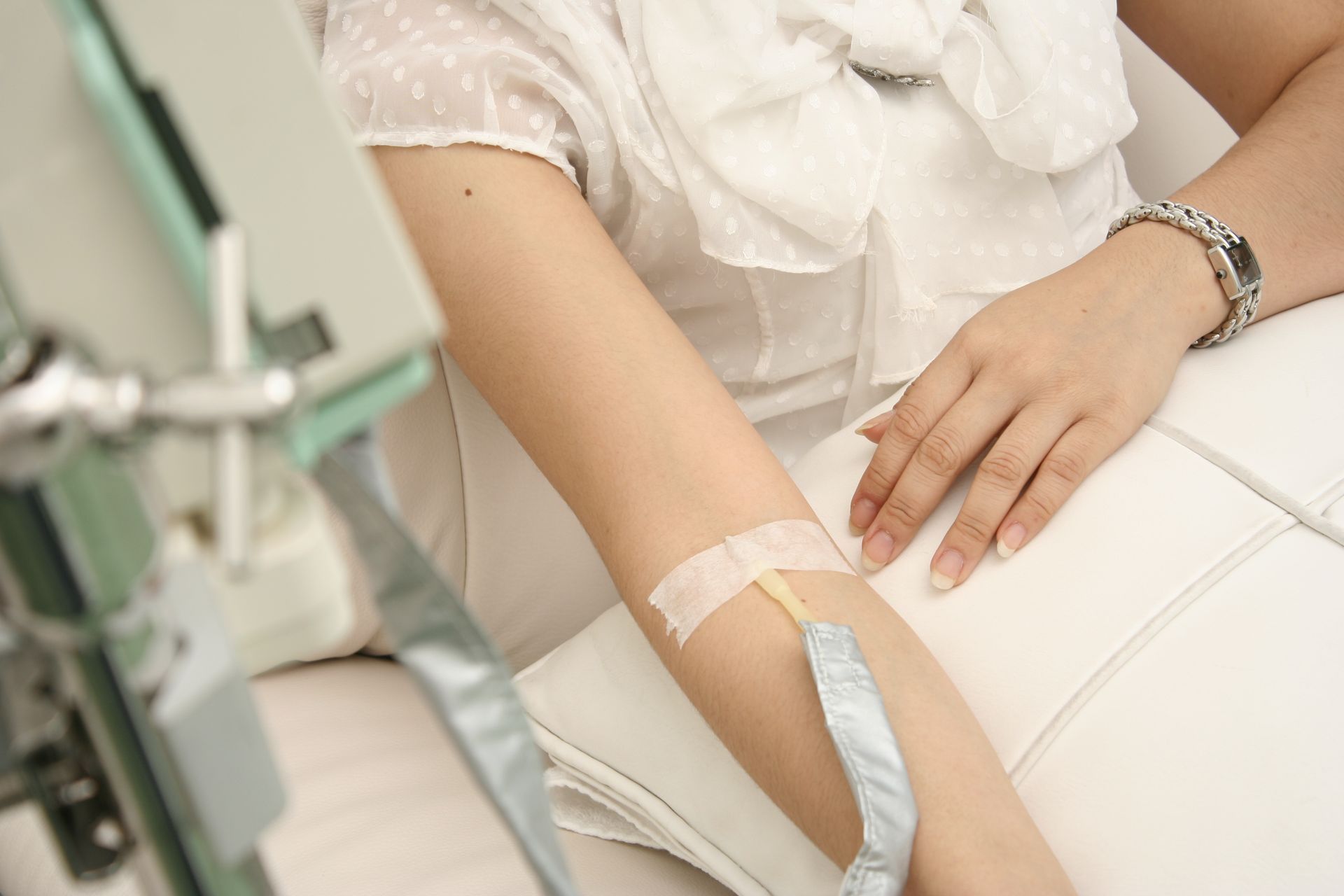 Arm with IV line resting on a white chair, suggesting a medical or donation setting