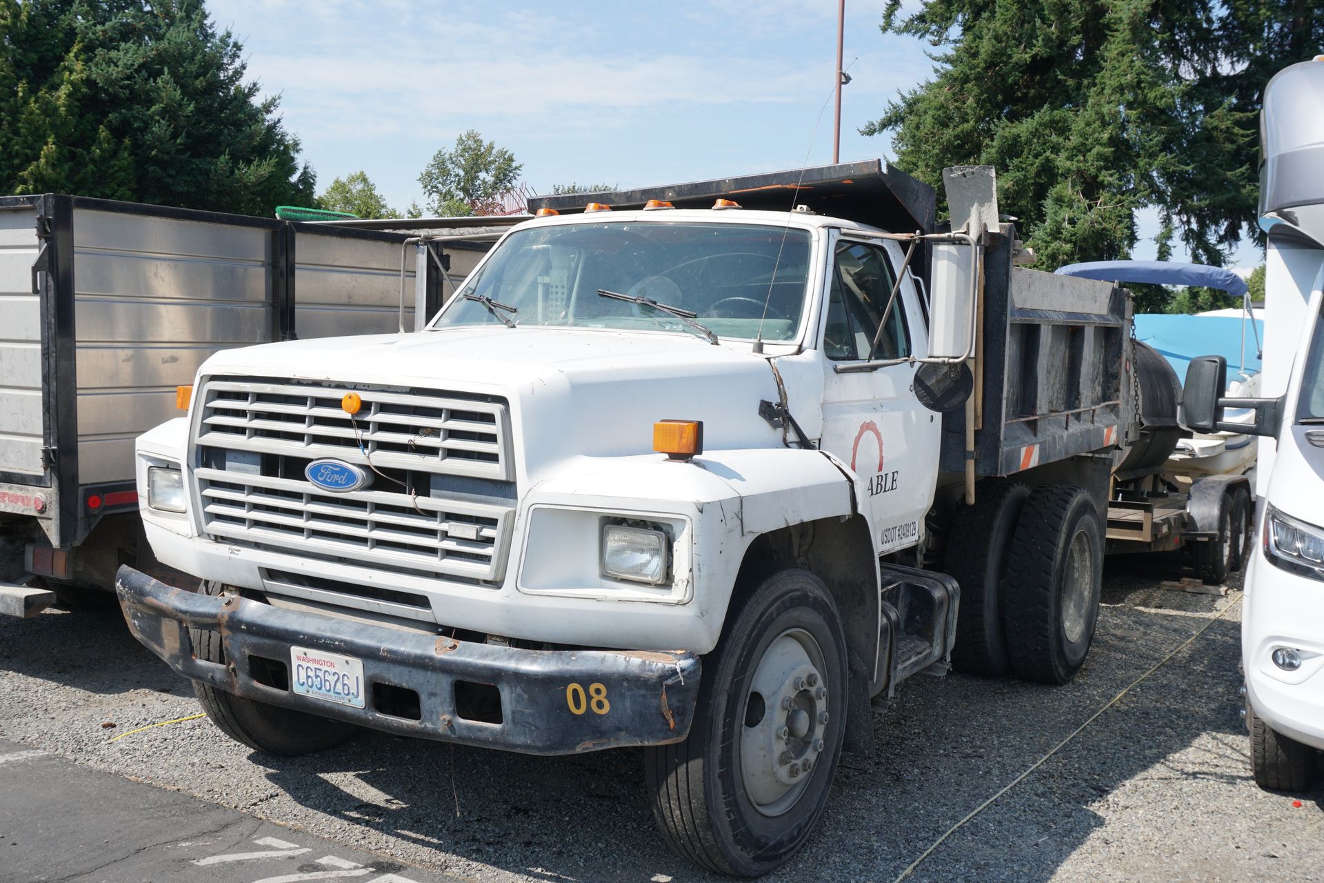 White Ford dump truck parked outdoors next to a trailer and a RV.