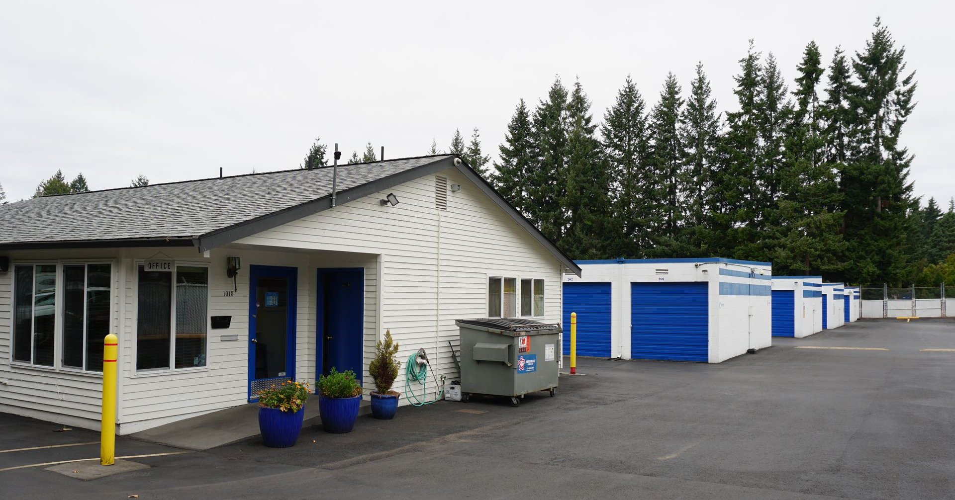 Storage facility with white building, blue doors, and rows of blue-doored storage units.