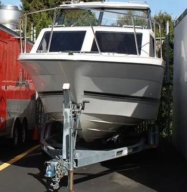 White boat on a trailer, parked between a red trailer and a white one.