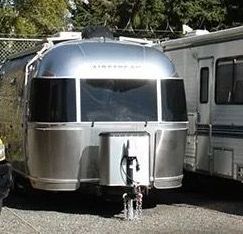 Shiny silver Airstream trailer with large front windows, parked next to a white RV.