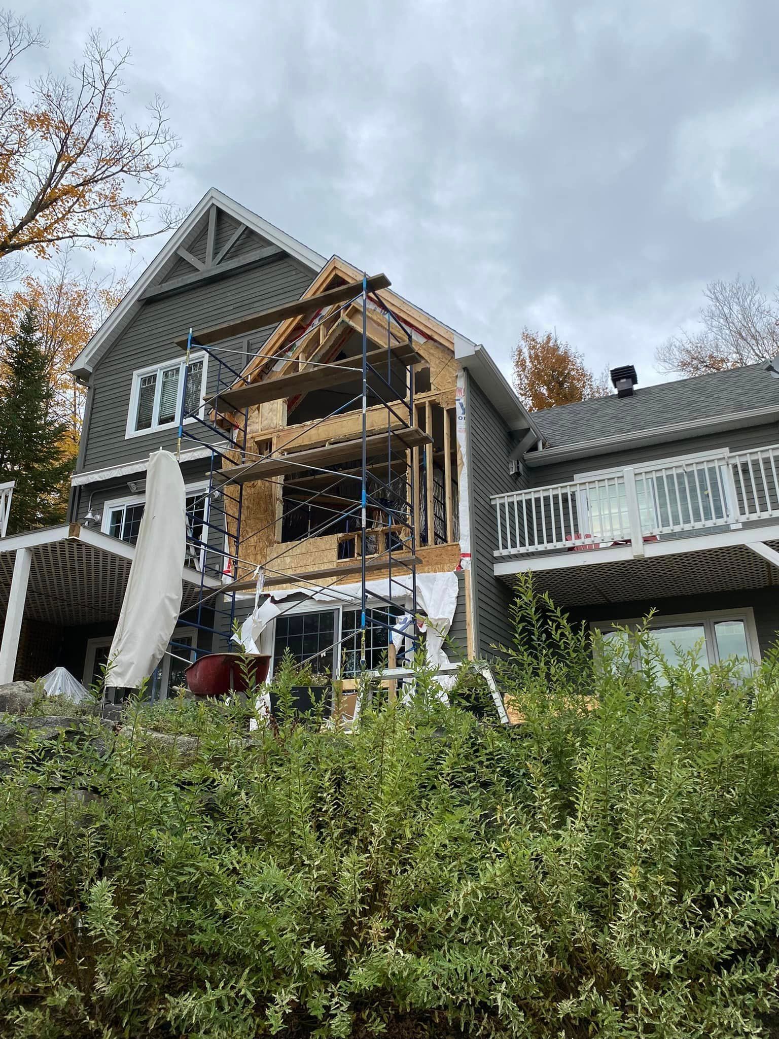 Une maison grise de deux étages en construction, avec des échafaudages autour d'une partie extérieure ouverte à ossature bois