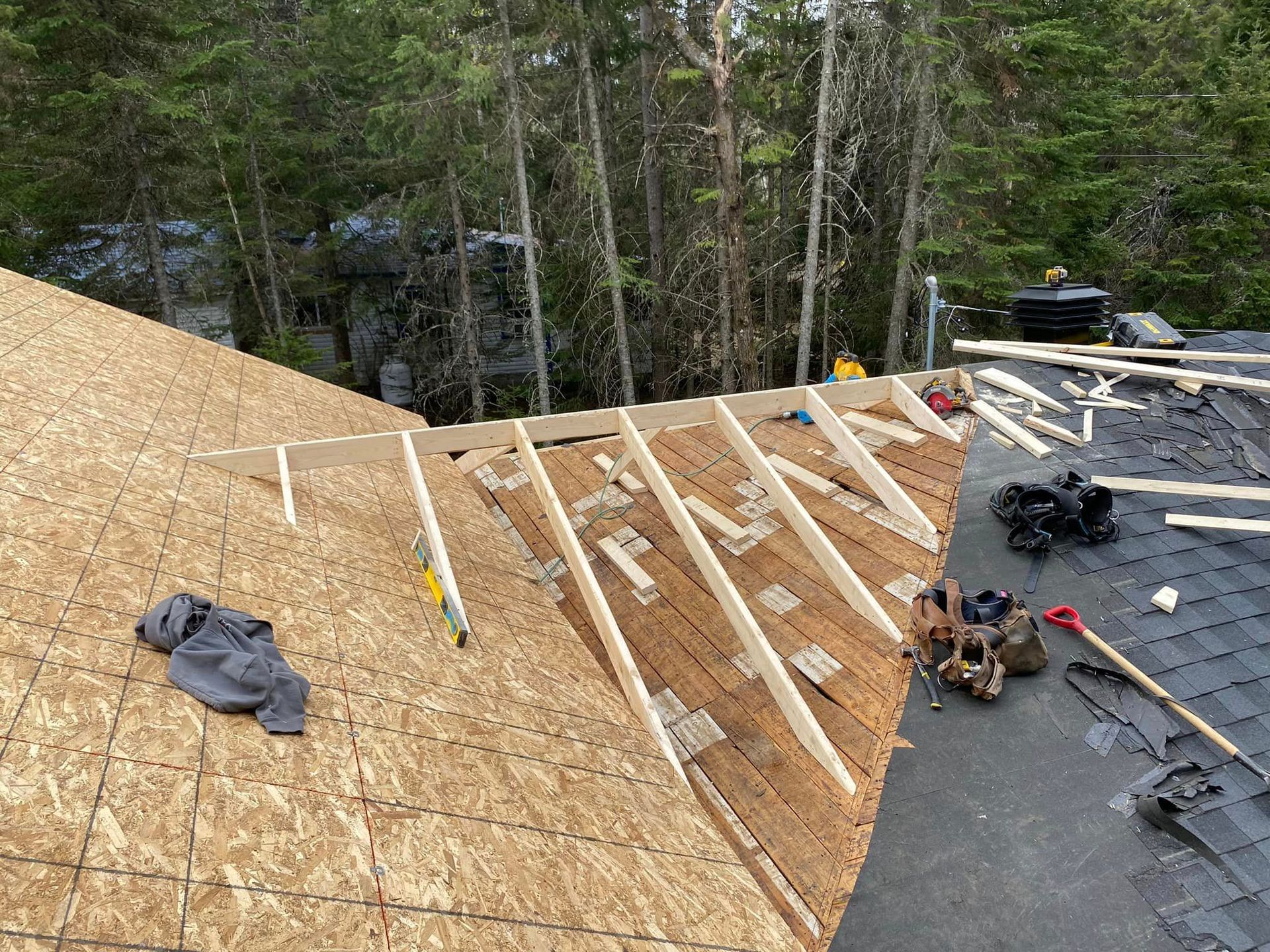 Un toit est en cours de construction avec des poutres en bois et des bardeaux.