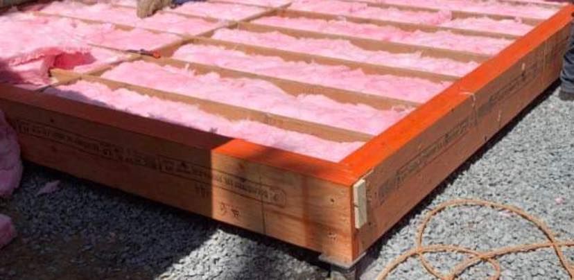 Une boîte en bois remplie d'isolant rose est posée sur le sol.