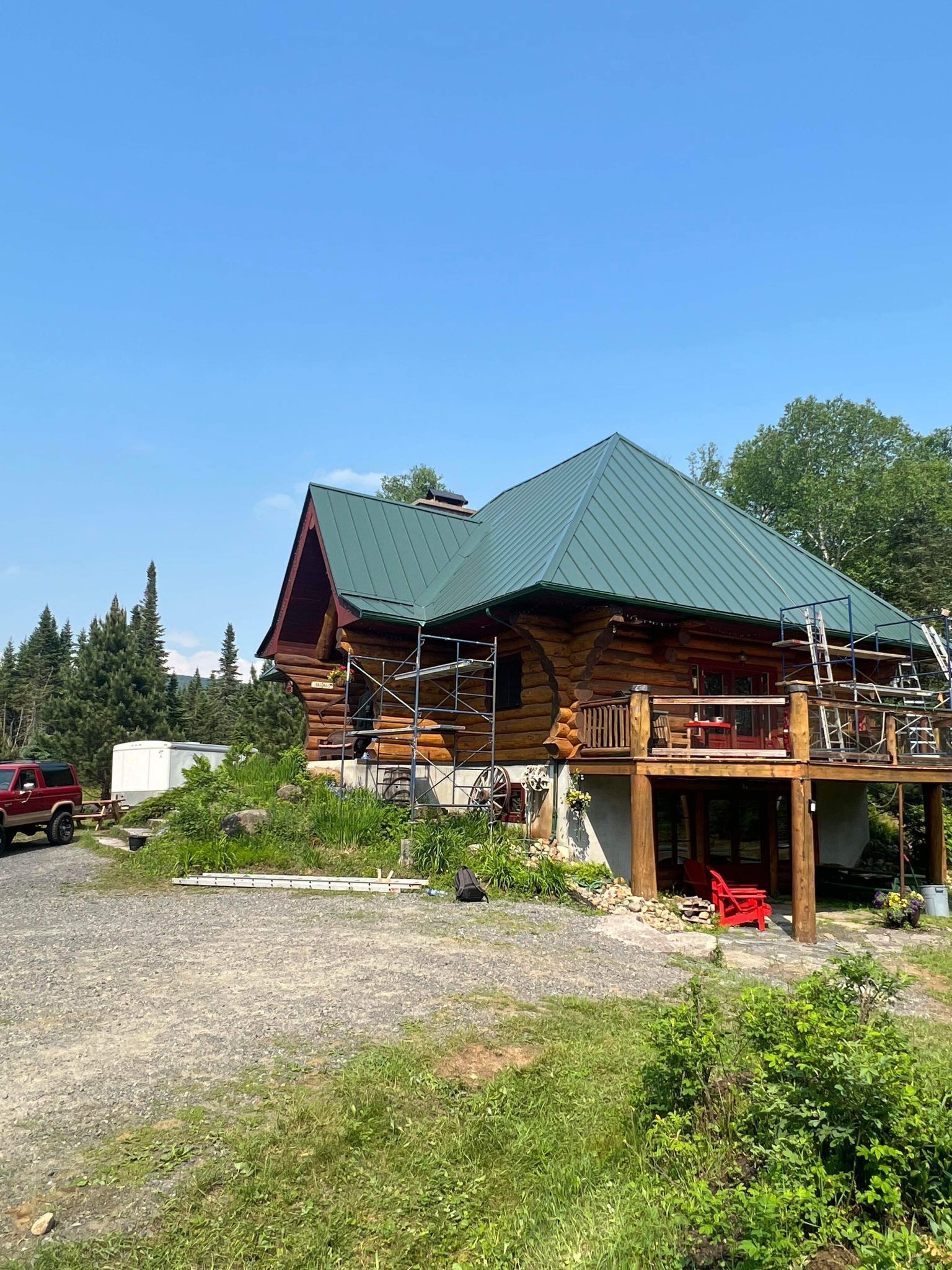 Une cabane en rondins avec un toit vert et un camion rouge garé devant.