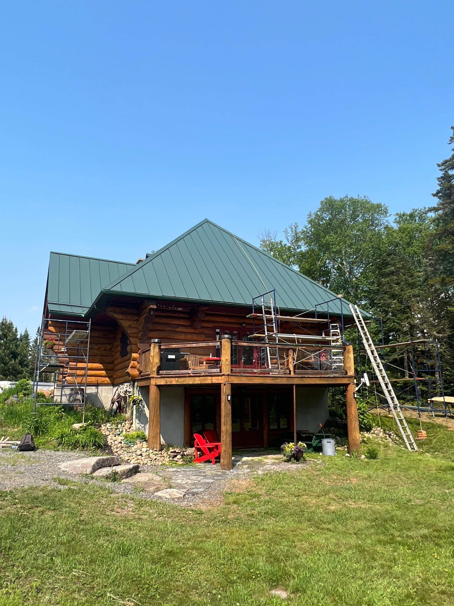 Une cabane en rondins avec un toit vert est située au sommet d'un champ vert luxuriant.