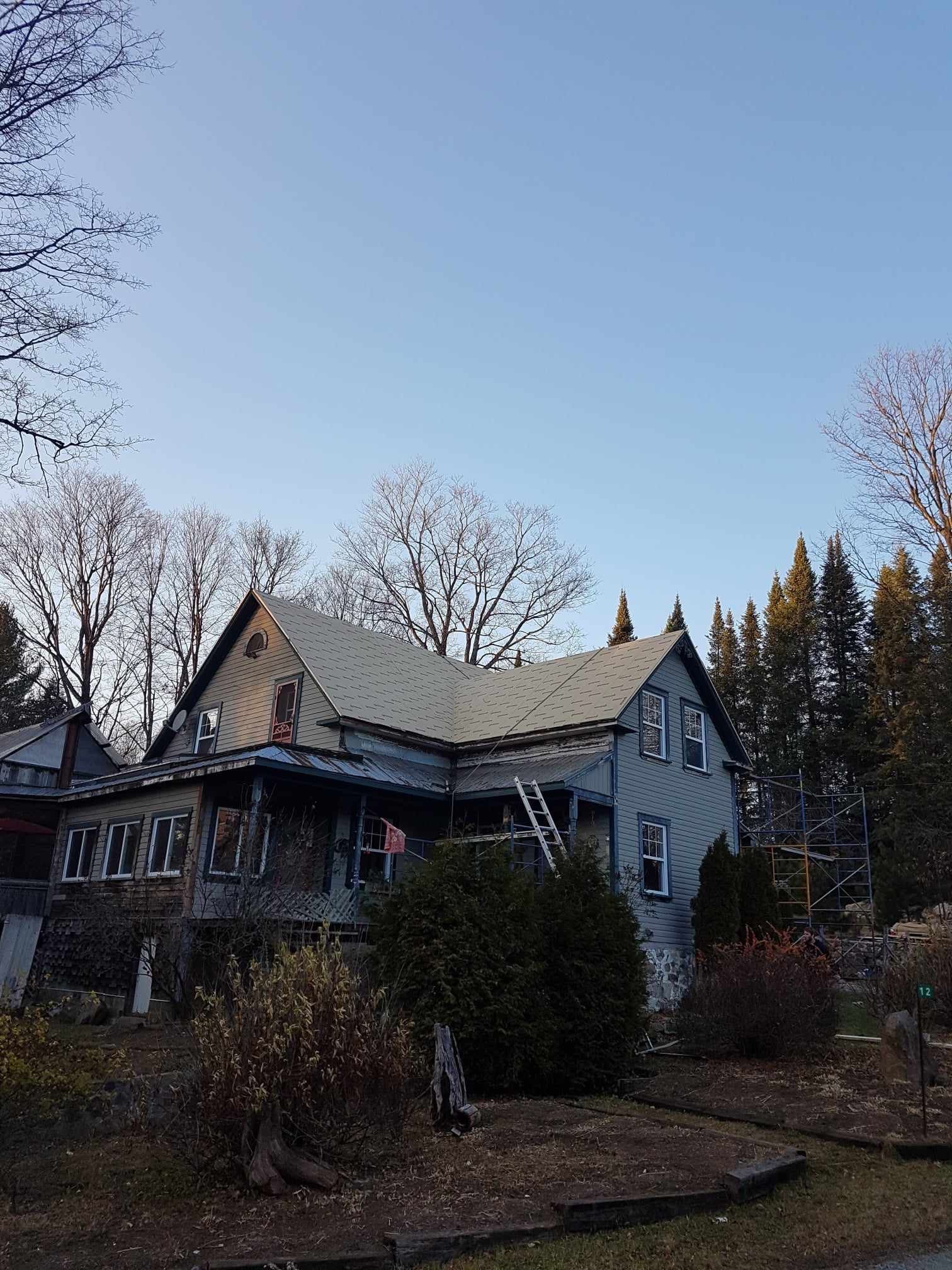 Une grande maison au toit blanc est entourée d'arbres et de buissons.