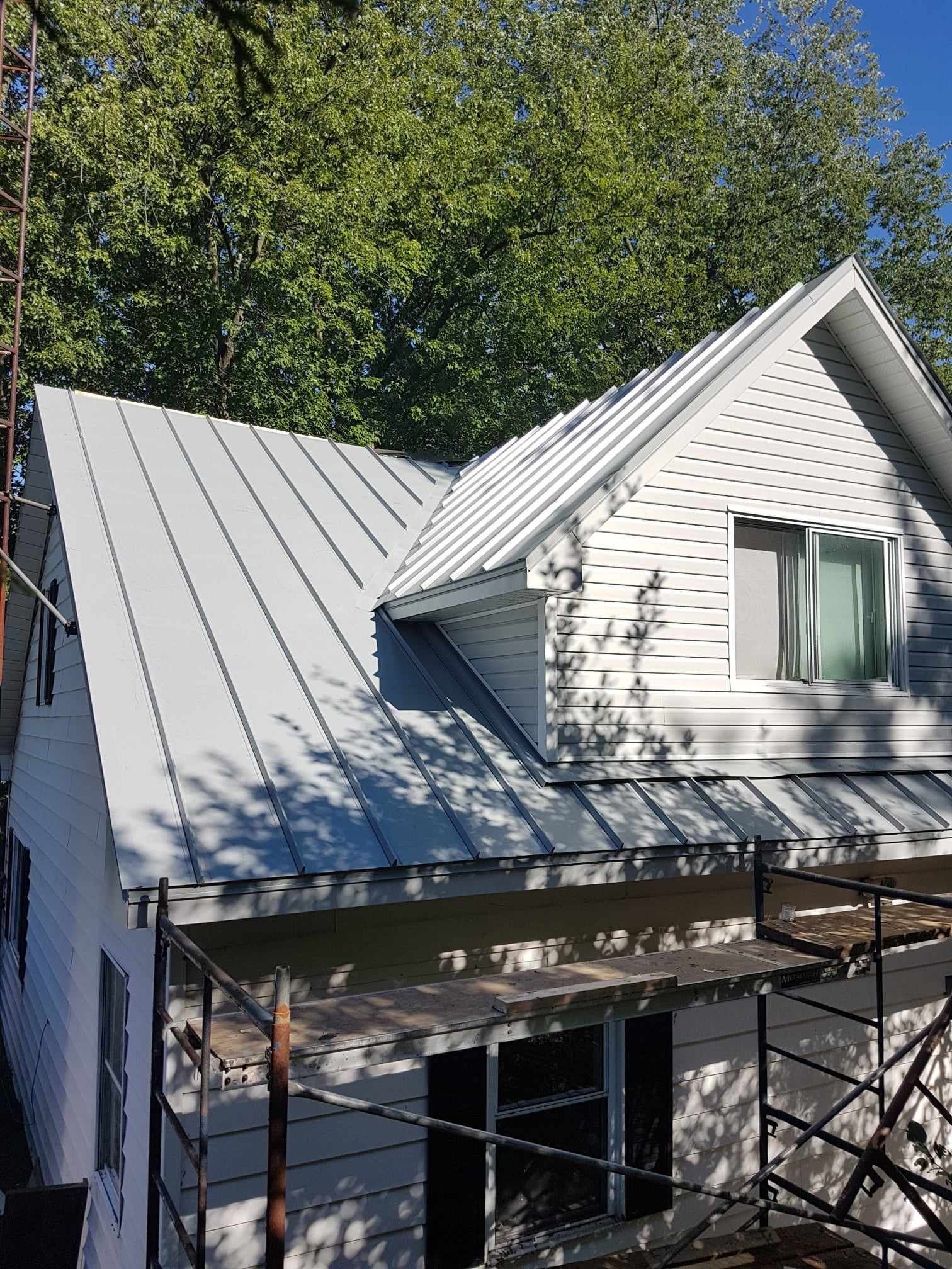 Une maison blanche avec un toit en métal et un échafaudage devant.
