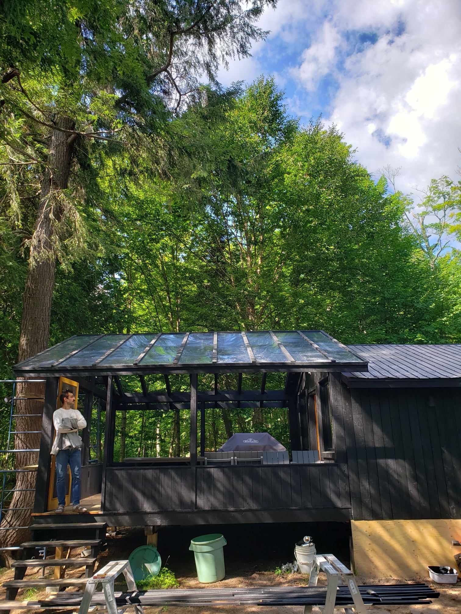 Une femme se tient debout sur une échelle devant une maison noire entourée d'arbres.
