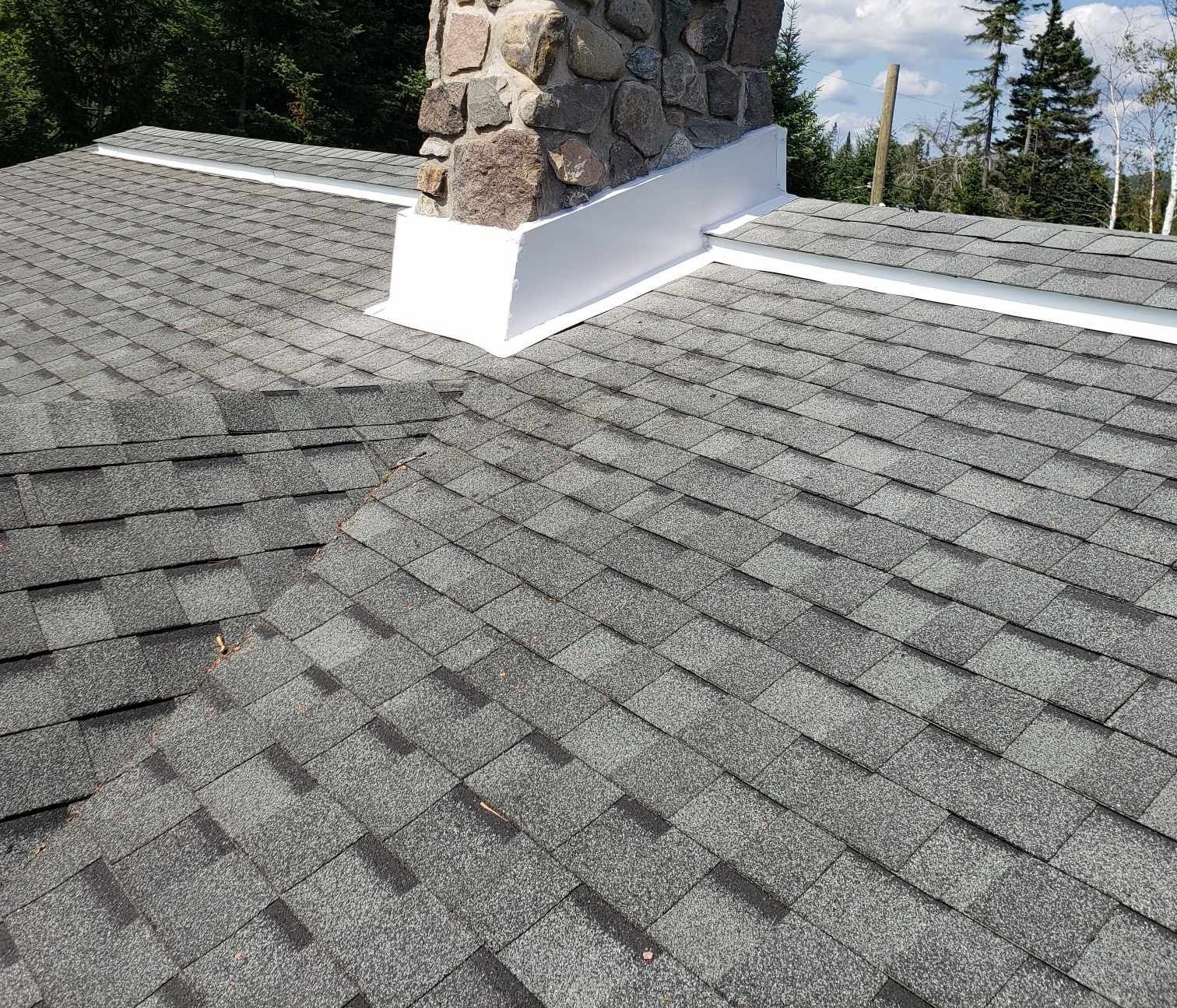 Toiture en bardeaux d'asphalte gris avec cheminée en pierre et solins blancs.