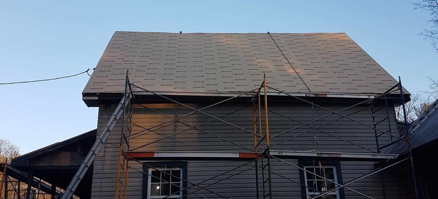 Maison en construction avec échafaudages et toiture en bardeaux neufs.