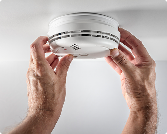 A person is installing a smoke detector on the ceiling.