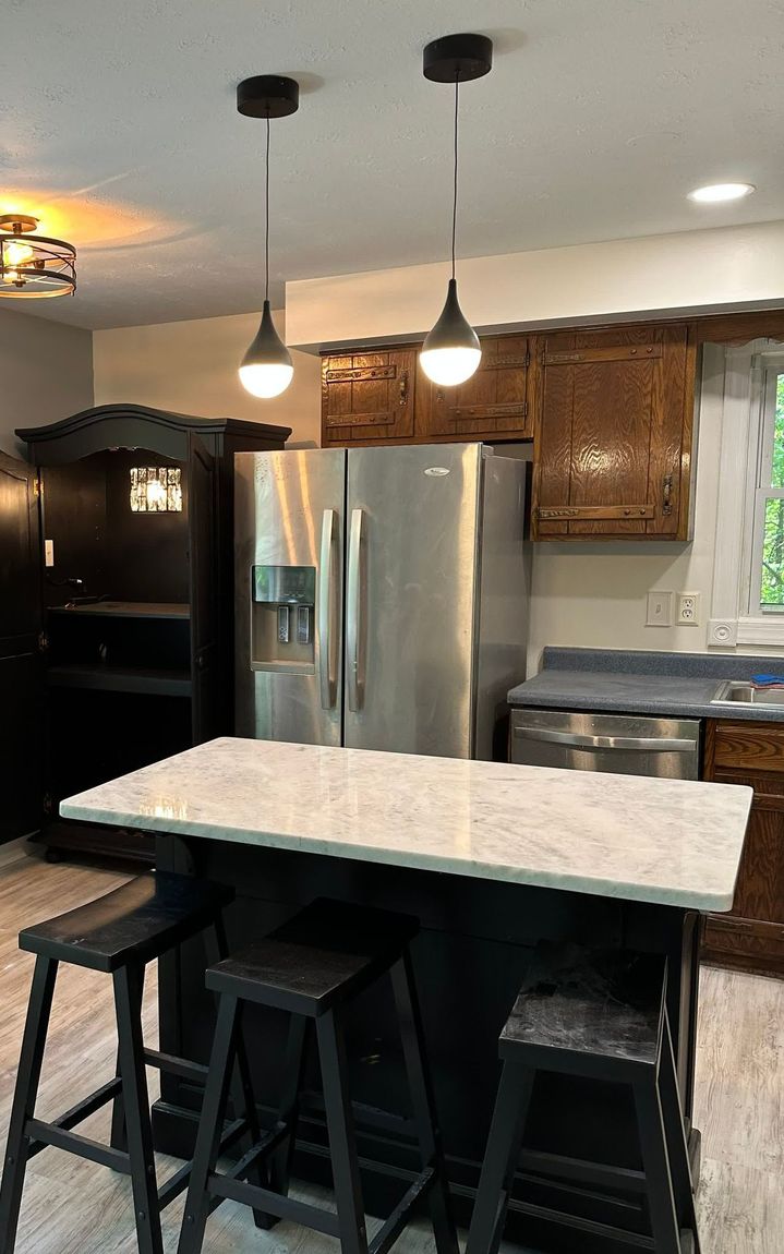 A kitchen with white cabinets , a stove , a refrigerator , a sink and a ceiling fan.