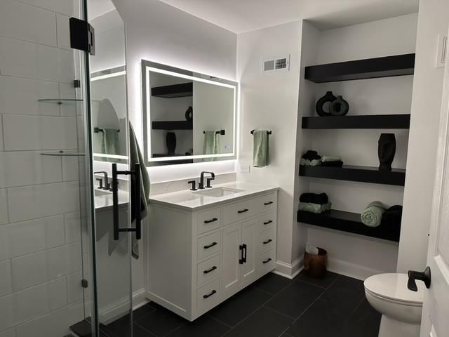 A bathroom with a toilet , sink , mirror and shelves.