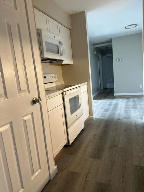 A kitchen with white cabinets , a stove and a microwave.