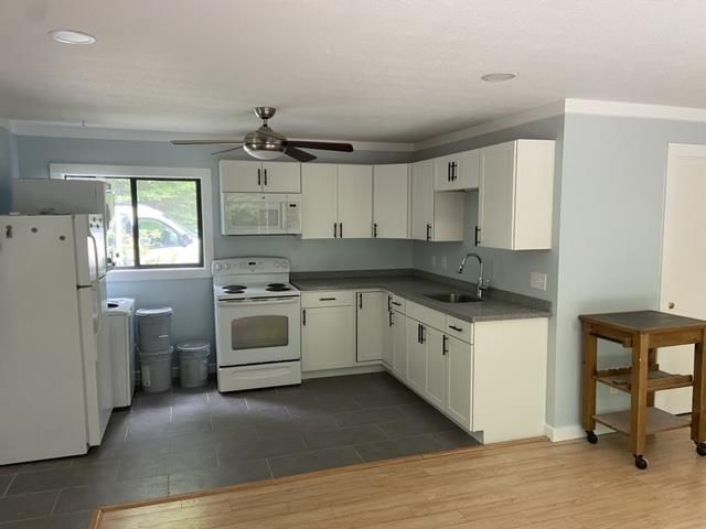 A kitchen with white cabinets , a stove , a refrigerator , a sink and a ceiling fan.