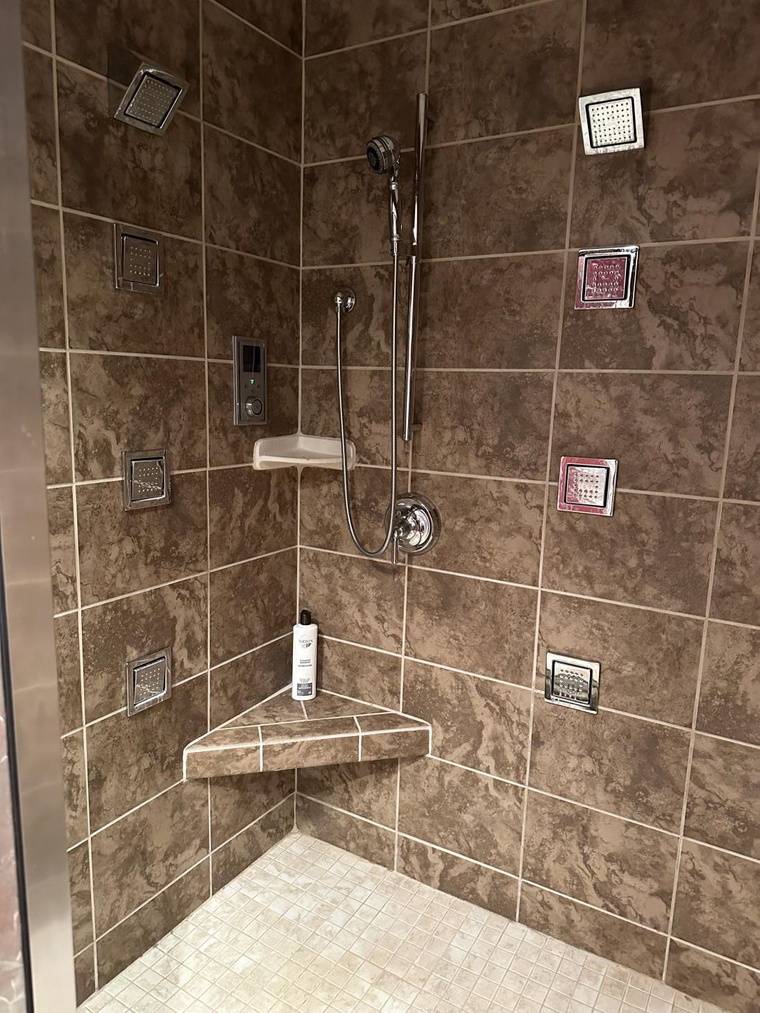 A shower with a corner seat and a shower head.