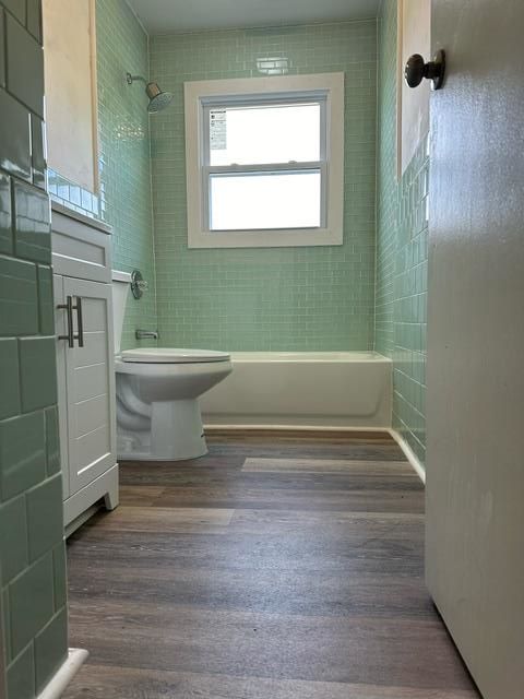 A bathroom with green tiles , a toilet , a tub and a window.