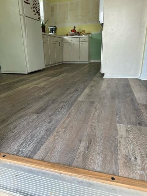 A kitchen with a wooden floor and a refrigerator.