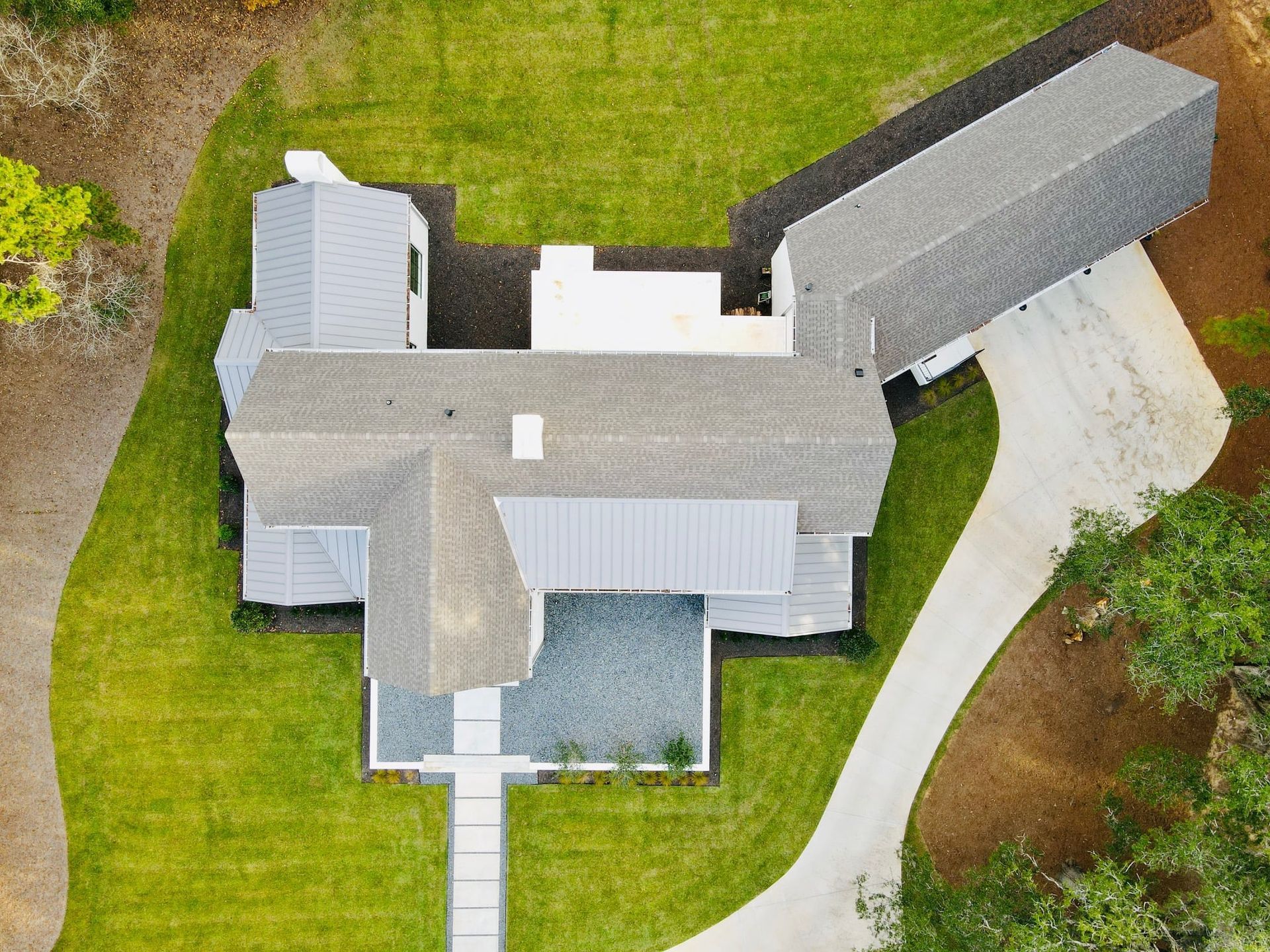 Overhead view of a modern house with gray roof, white walls, and a long driveway on green grass.