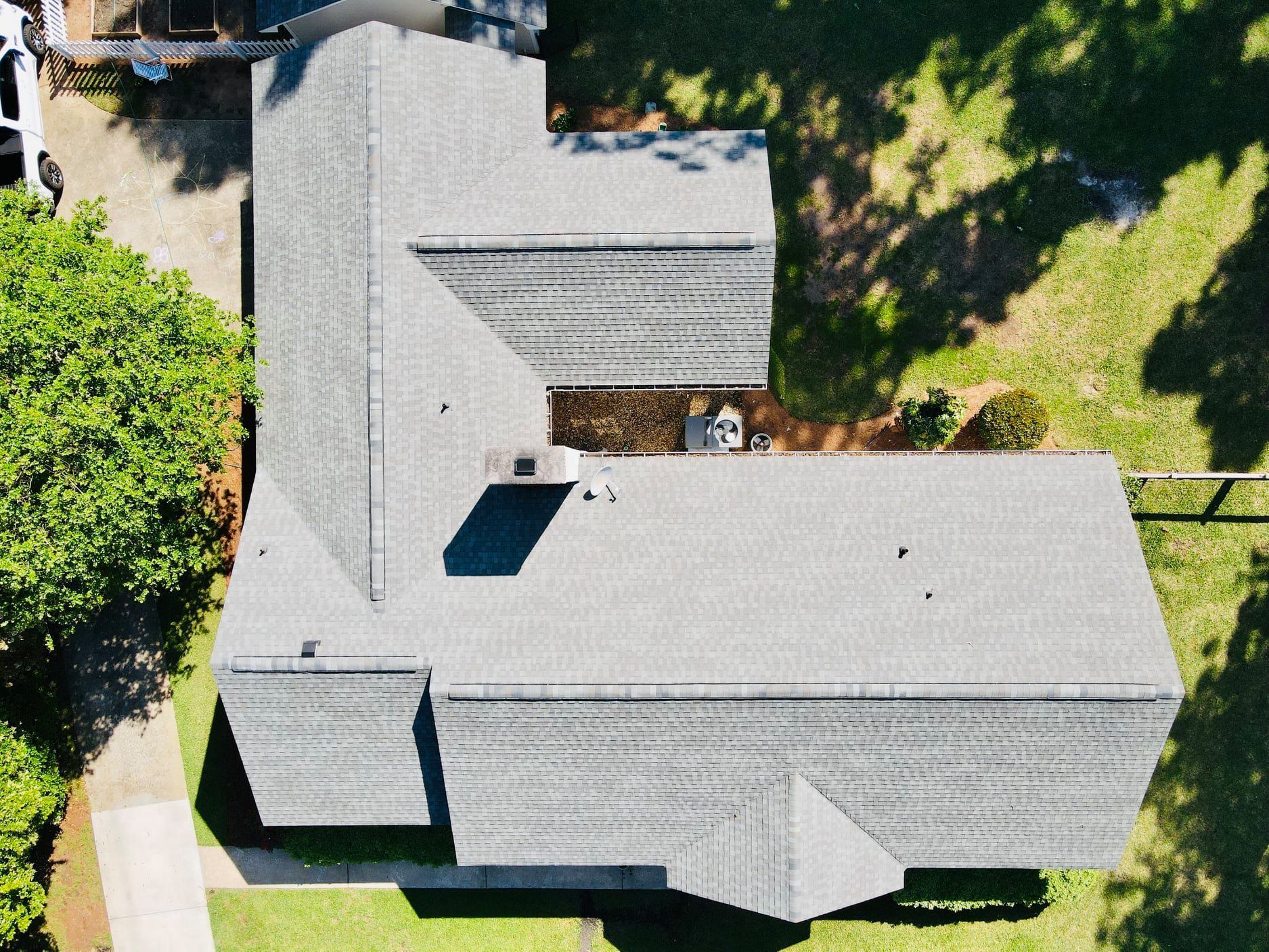 Overhead view of a gray-roofed house with an L-shaped design, surrounded by grass and trees.
