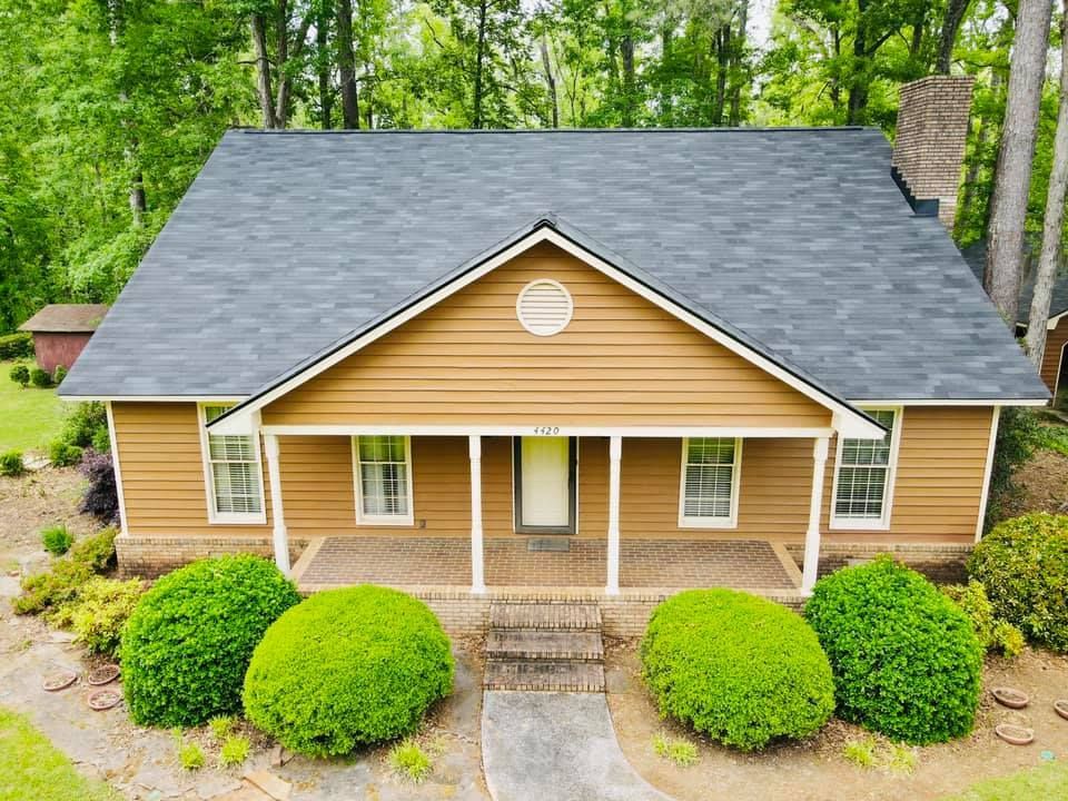 Tan house with dark gray roof, front porch, and green bushes.