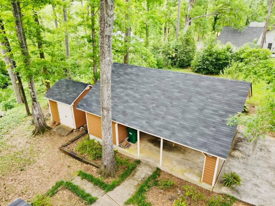 Beige and brown house with a carport and shed nestled among green trees.