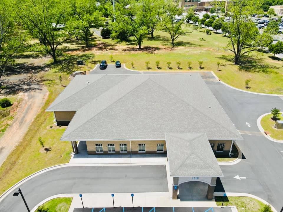 Aerial view of a light-colored building with a large gray roof and a circular driveway.