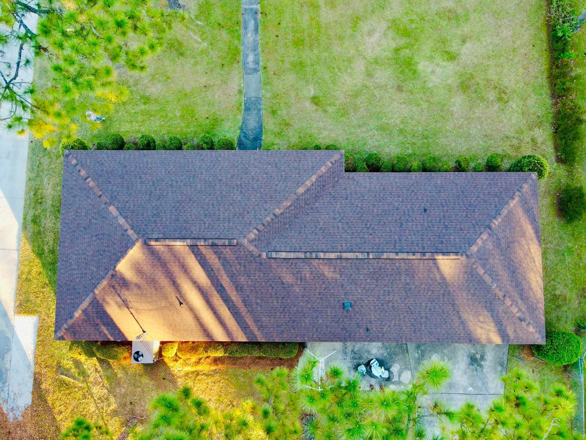 Overhead view of a house with brown roof, surrounded by green grass and trees.