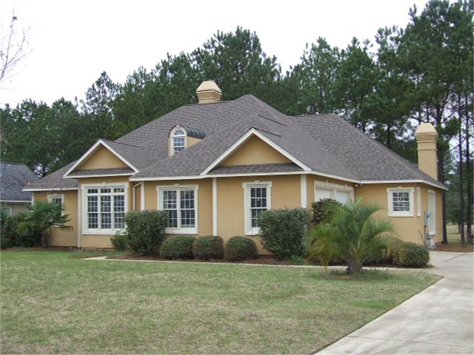 Yellow stucco house with brown roof and chimney, white trim, and a green lawn.