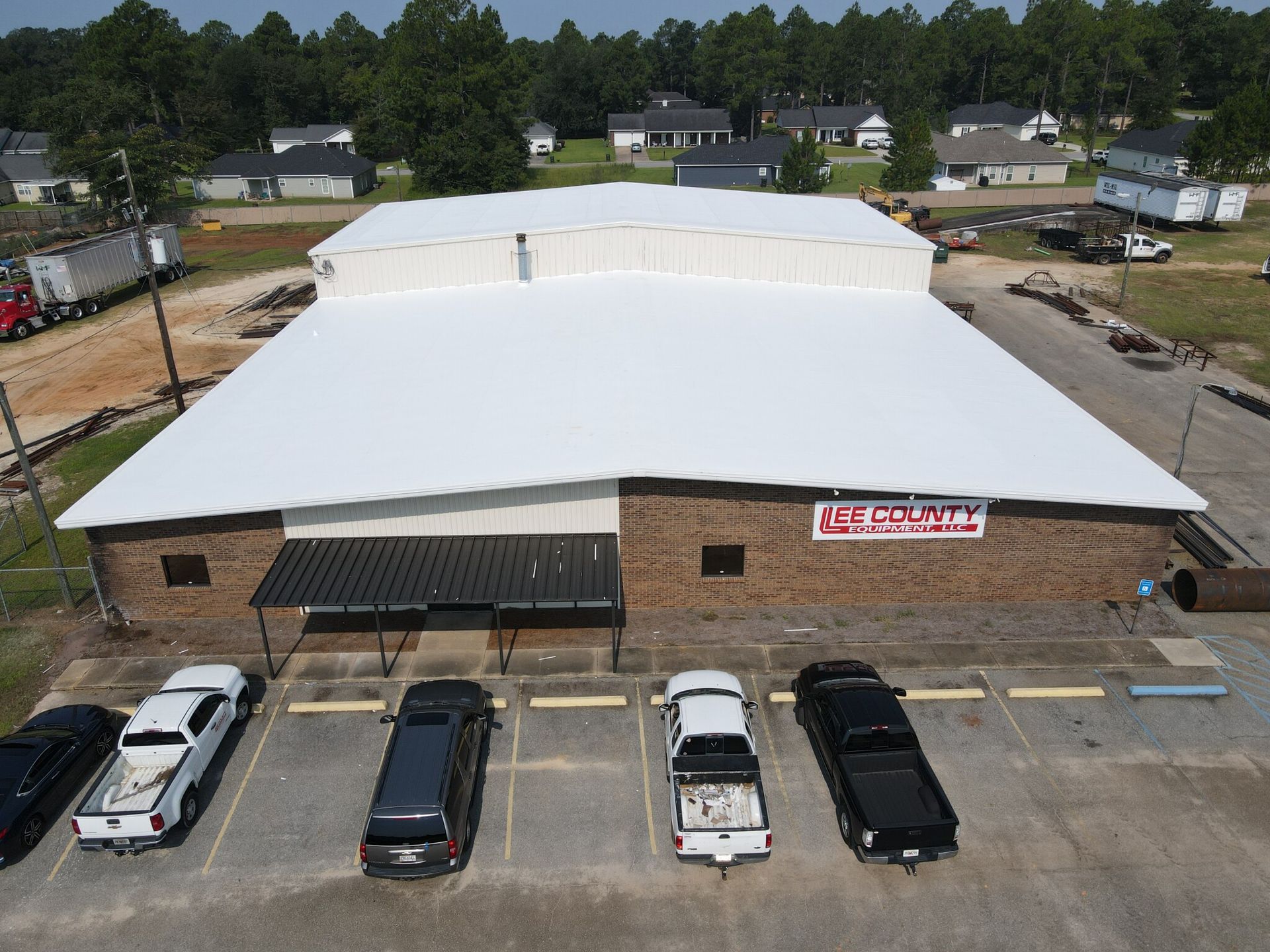 Large, white-roofed brick building with a black awning and parked vehicles in front; in a residential area.