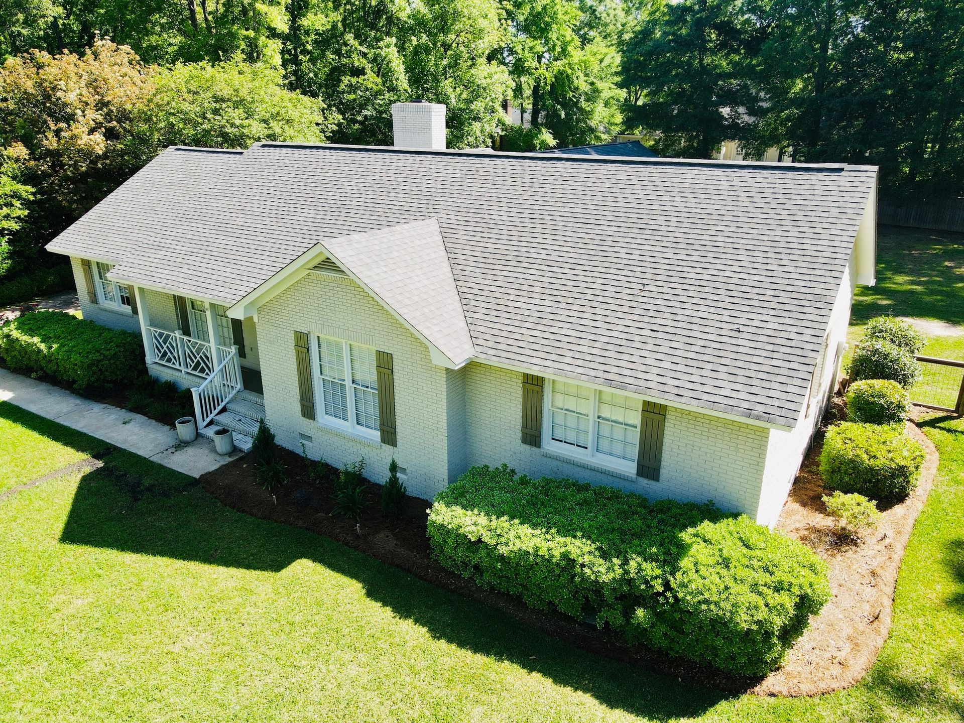 Cottage-style house with gray roof and light-colored siding, surrounded by green grass and shrubs.