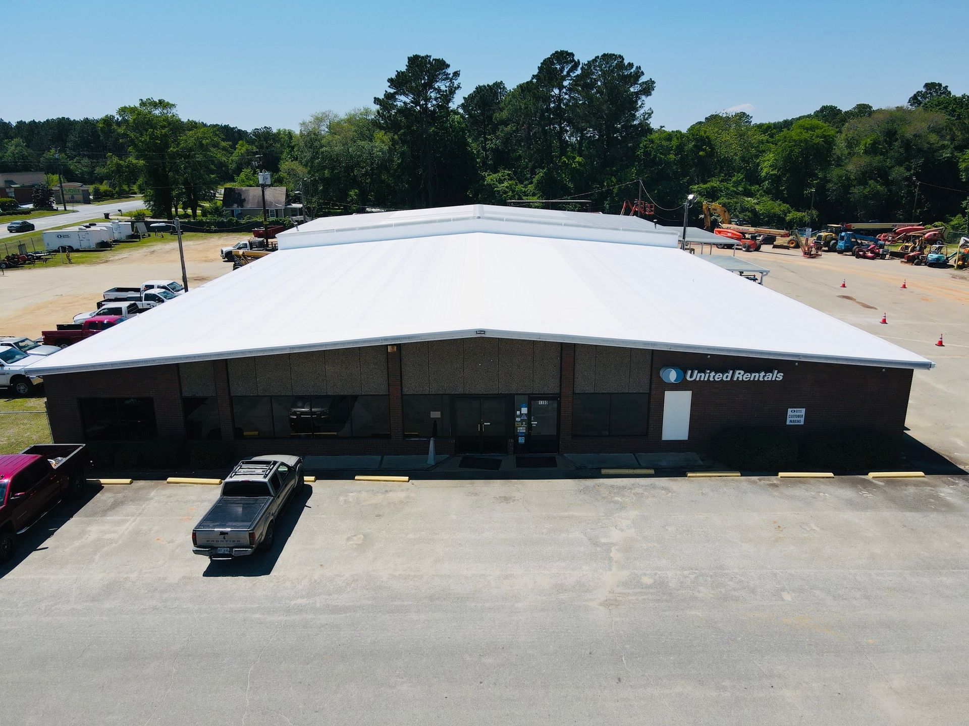 A one-story commercial building with a white roof and brick facade; surrounded by vehicles and equipment.