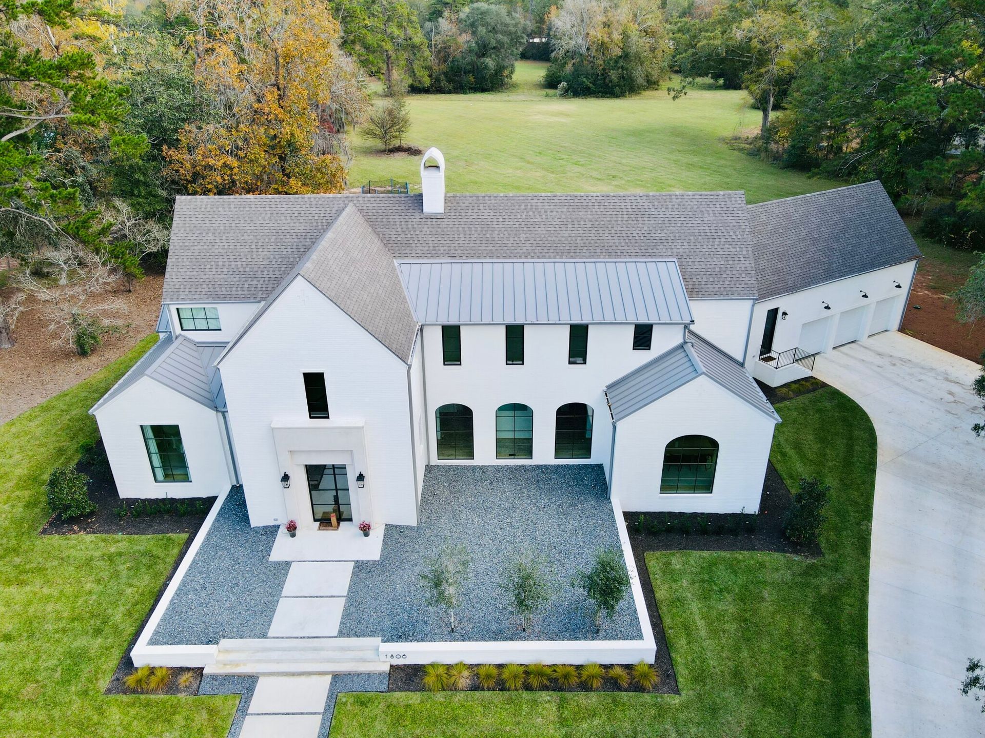 Tan house with a dark roof, green lawn, and tall trees in the background.