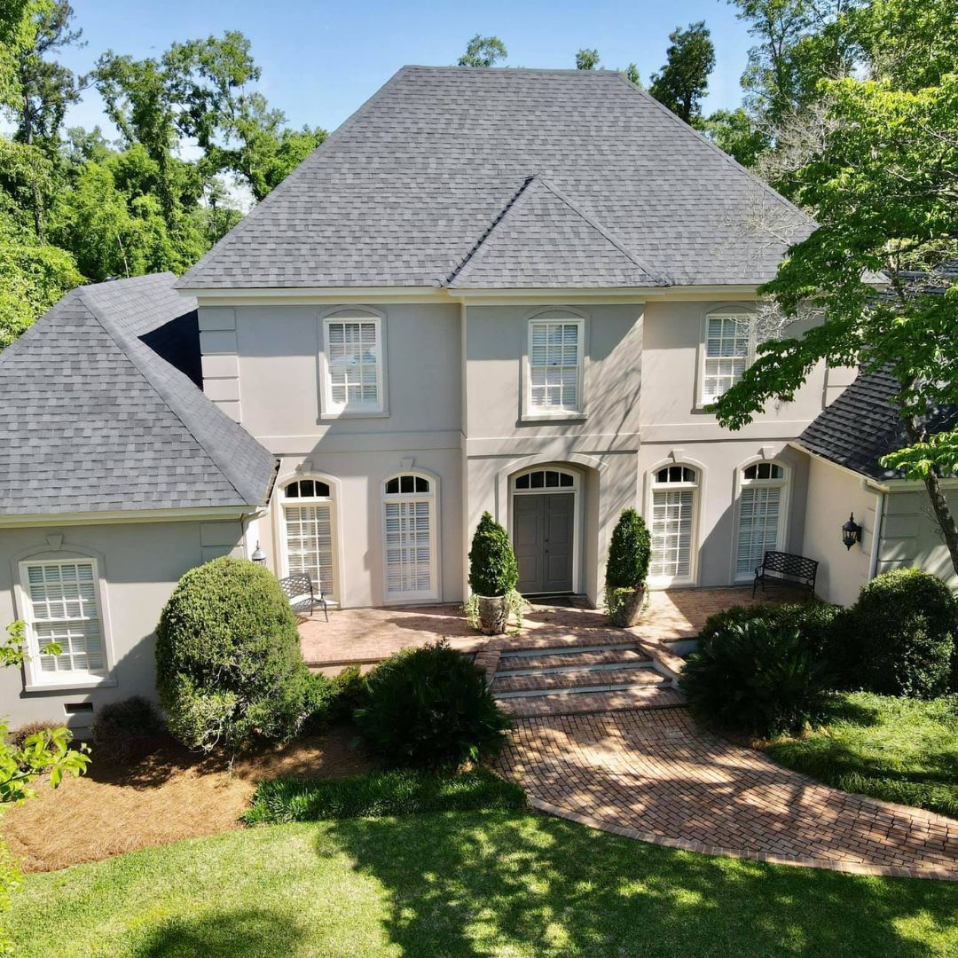 Gray stucco house with dark gray roof, symmetrical design, brick path, landscaping.