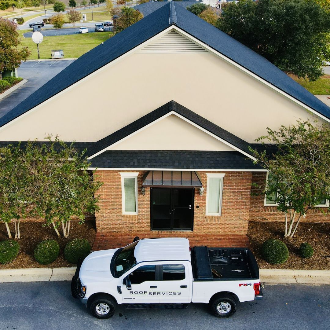 White truck parked in front of a brick building with a dark blue roof. Trees and shrubs surround the building.