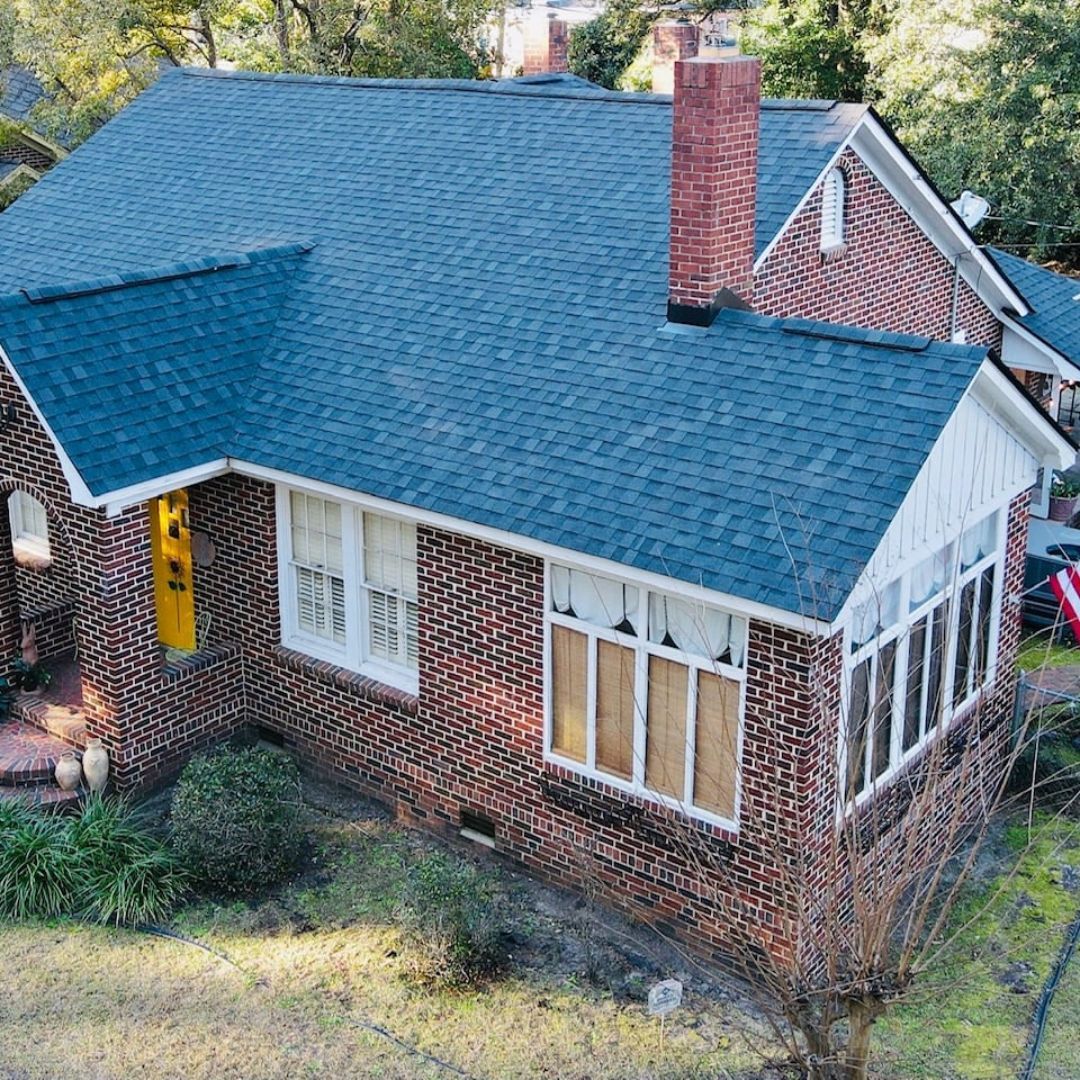 Brick house with blue roof, yellow door, white trim, and a brick chimney.