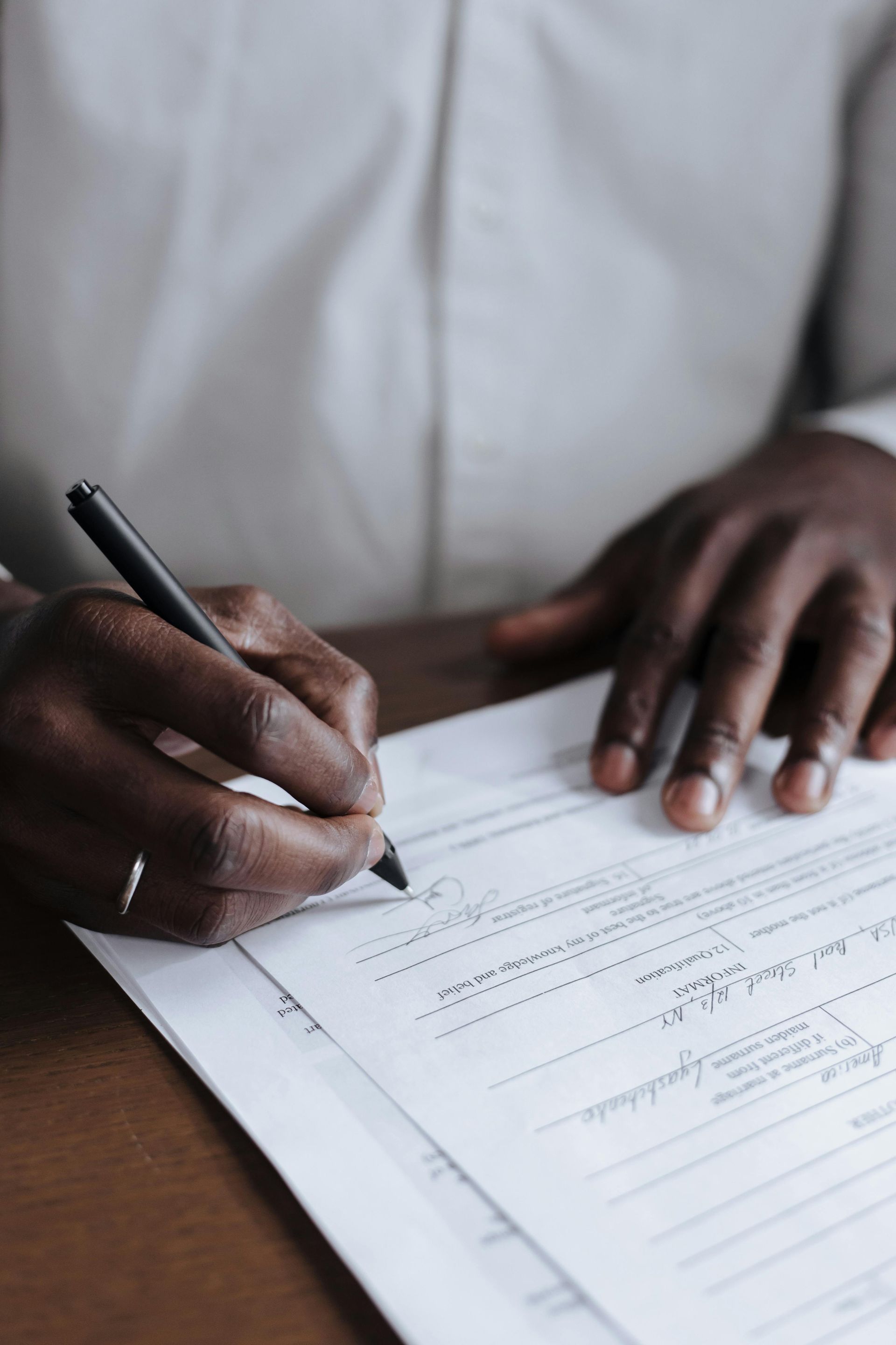 Person of color signing paperwork with a black pen; close-up.