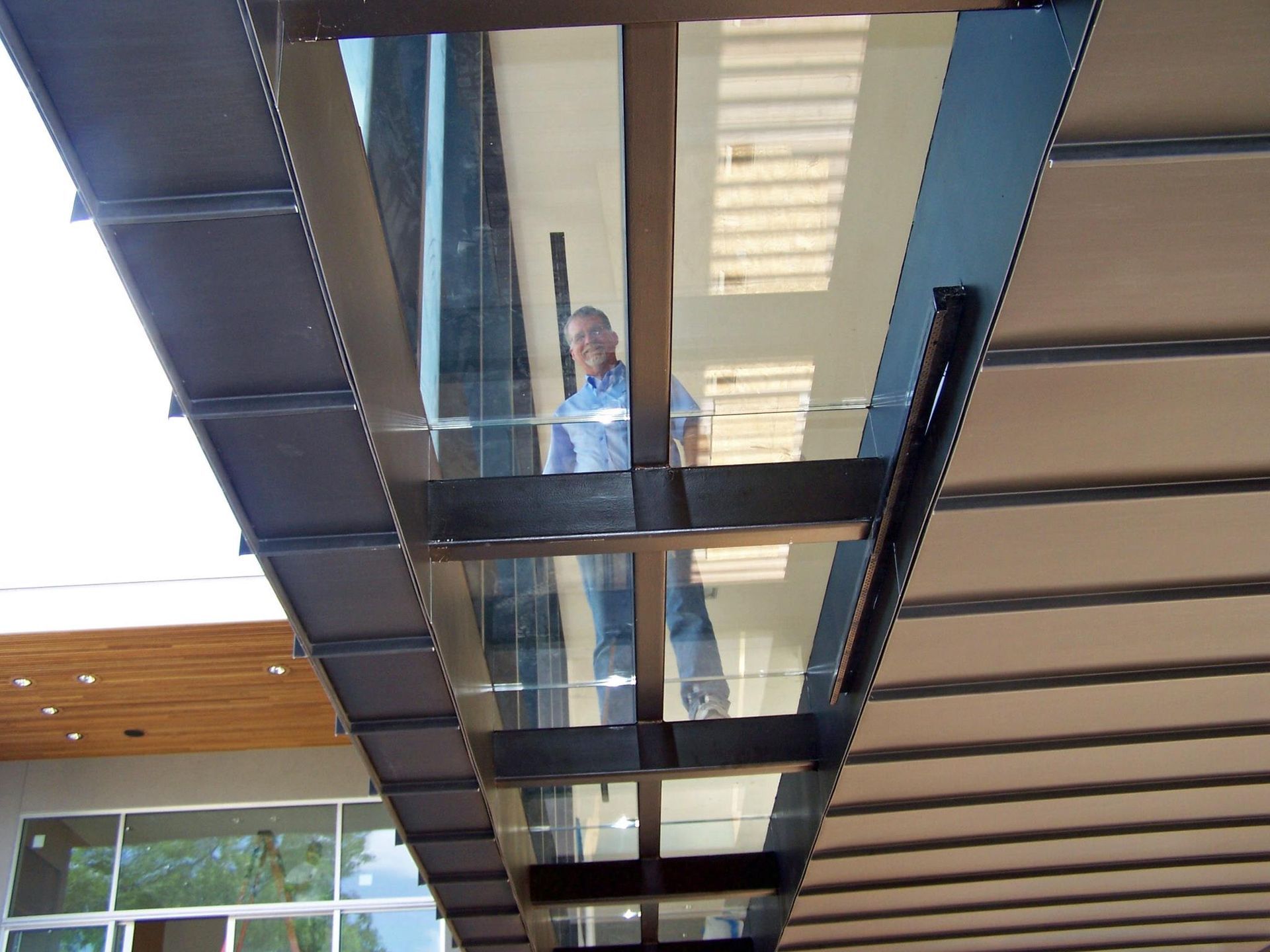 A man in a blue shirt is standing under a glass bridge